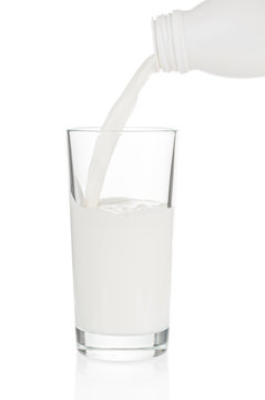 Pouring milk from plastic bottle in glass on white background
