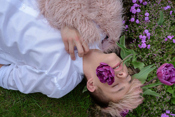 Young sexy man in a white clothes and pink coat poses in a park with flowers. Fashion concept