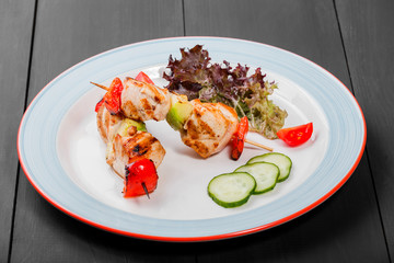 Grilled meat kebabs on skewers with vegetables, cherry tomato, pepper, zucchini in plate on dark wooden background