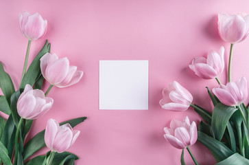 Pink tulips flowers and sheet of paper over light pink background. Saint Valentines Day frame or background. Greeting card or wedding invitation. Flat lay, top view, copy space