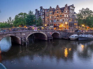 Fototapeta na wymiar Amsterdam canal, bridge and typical houses, boats and bicycles during evening twilight blue hour, Holland, Netherlands.