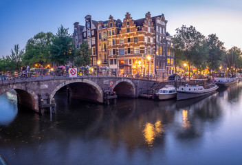 Fototapeta na wymiar Amsterdam canal, bridge and typical houses, boats and bicycles during evening twilight blue hour, Holland, Netherlands.