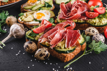 Various of sandwiches and bruschetta with prosciutto, fried quail egg, avocado, cucumber, tomatoes, spices and greens