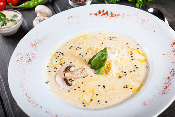 Cream soup with mushrooms, herbs, cheese parmesan, basil, sesame on plate on dark wooden background. Homemade food