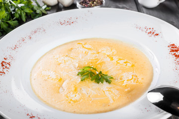 Cream soup with cheese parmesan, herbs and chicken on plate on dark wooden background. Homemade food. Ingredients on table