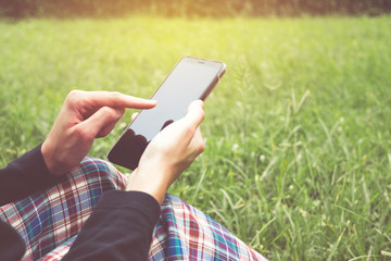 Closeup hand of female holding smartphone siting on grass and looking some concept for technology in nature background.