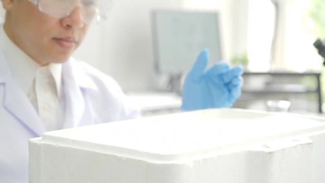 Medical research scientist takes out petri dish with frozen samples of cells from a cryogenic nitrogen container in a science research lab. He works in a busy modern laboratory center.
