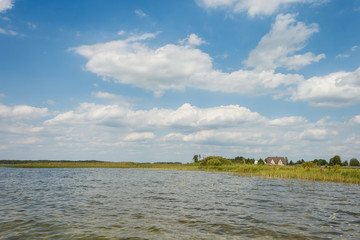 Lake on a sunny day with blue sky and white clouds. View from the water, to the shore cottages.