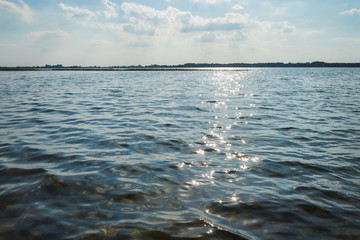 Waves and glare on the surface of the water. Lake on a sunny day with blue sky and white clouds
