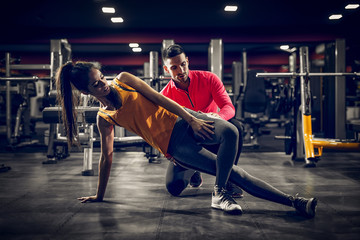 Young tired woman stretching her muscles with a help of her coach.