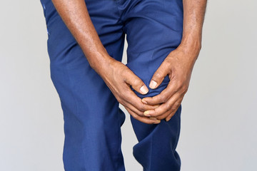 Pain In Knee. Close-up African Male Leg With Painful Kneeson on gray background. Man Feeling Joint Pain, Having Health Issues And Touching Leg With Hands. Body And Health Care Concept.