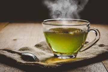 Poster Im Rahmen Close-up a cup of green tea on sackcloth, hot drink with steam © Thitiwat.Day