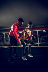 Fototapeta premium Young fit female is doing dead lifts with a help of her coach.
