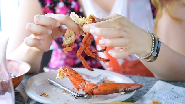 Closeup of lobsters and seafood on plate, platter with woman, female person eating crab leg with hands on table in restaurant, cafe outside, outdoors
