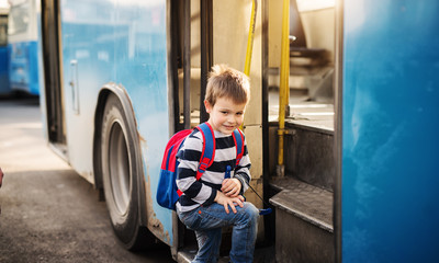 Cute small boy is entering a bus with a school bag on his back.