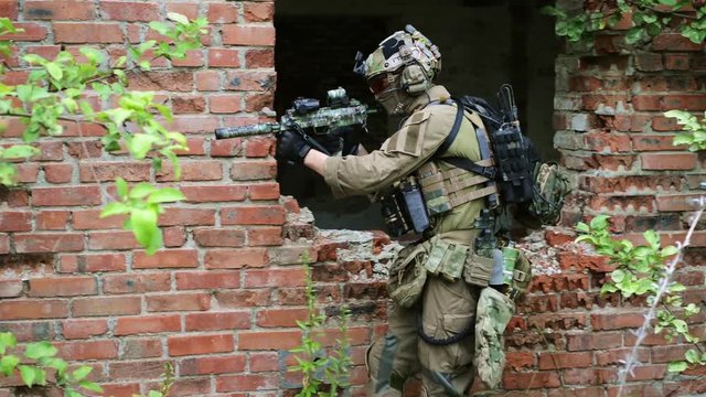 Airsoft men in ammunition with gun along the wall