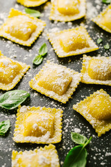 Raw ravioli with basil and flour on dark