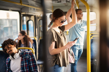 Sweet girl with sunglasses in using phone while standing in a bus.