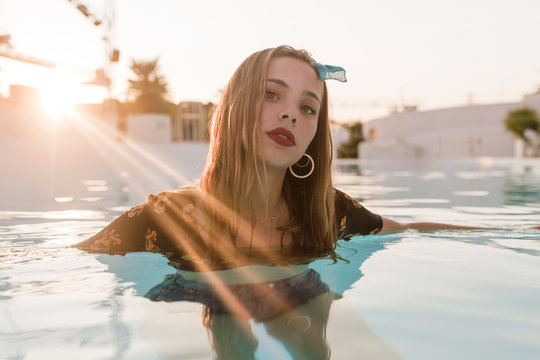 Young blond vintage girl with denim short pants and bandana posing and moving by the water on a pool in a sunset of a sunny day of summer
