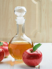 A bottle of apple cider vinegar close-up and a row of red apples with green leaves