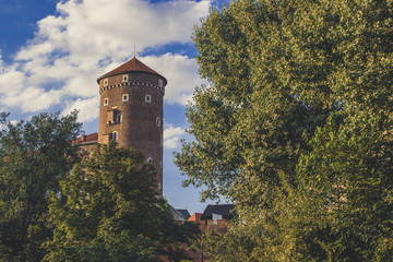 old medieval brick red castle tower between green trees on blue sky cloud background with empty space for copy or text