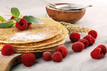 Homemade crepes served with fresh raspberrries and powdered sugar on rustic table.