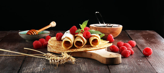 Homemade crepes served with fresh raspberrries and powdered sugar on rustic table.