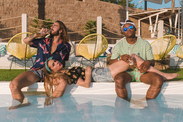 Three friends relaxing and drinking beer in a pool in a sunset of a sunny day of summer