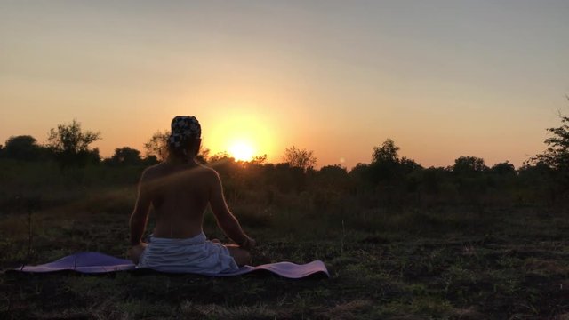 Sunset, the Young man does yoga, practices meditation, the rear view of the back and a naked torso of a man, bright beautiful rays of the setting sun, hands Jnana the wise, white tabard