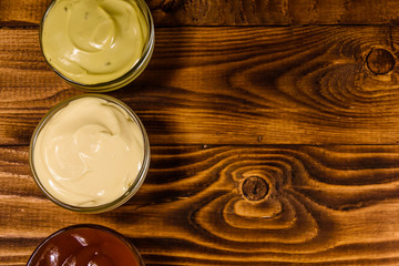 Different sauces in glass bowls on wooden table. Top view