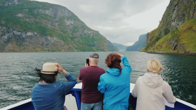 A group of tourists on the nose of a cruise ship. Enjoys the fjord in windy weather