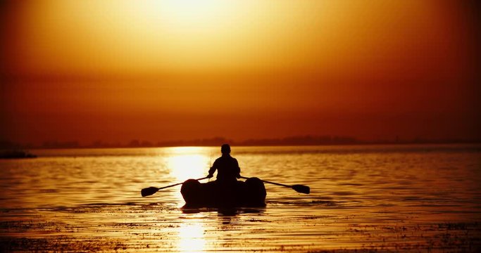 experienced Fisherman rowing with paddles in a rubber boat in a lake in sunset 4k