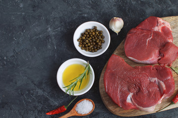 Fresh raw meat beef steak olive oil Spices Hot Salt Wooden spoon Chili Pepper Garlic Rosemary Cooking concept Cooking concept Dark concrete background Top view Copy space Flat lay