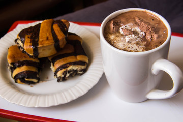 White cup with coffee on a tray with a plate with rolls with pop