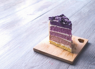 A slice of homemade purple ombre layer cake, vanilla layer cake with violet and withe buttercream frosting, on the wooden plate that on the grey wooden table with copy space.