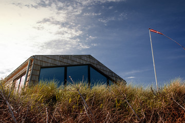 Danish modern holiday house with sea view in the grass and sand dunes and the Flag of Denmark....