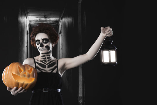 Portrait of woman with halloween skeleton makeup holding pumpkin and lamp