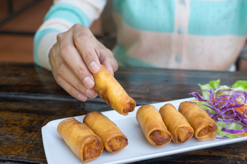 Girl eating spring rolls by using hand.