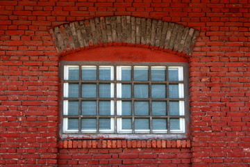 New window with safety wire protection, white frame, new window blinds and strong metal bars mounted on old red brick wall with decorative top in form of brick arch