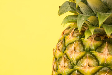 A close up of the tough, textured outer skin and leaves of a fresh pineapple on a yellow background with copy space.