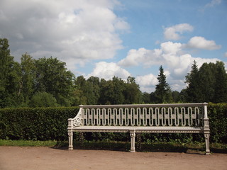 vintage white bench in the Park on the background of trimmed bushes, trees and cloudy sky