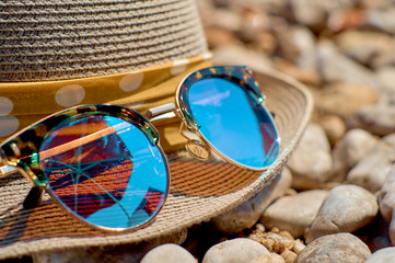 Hat with sunglasses on a pebble beach at the blue sea
