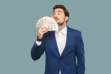 Handsome businessman in blue jacket standing and holding many dollars in hand and smelling and...