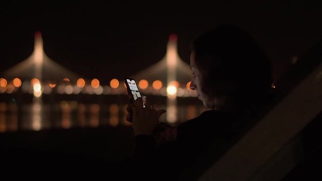 Young attractive lady sitting in the night park and wathing social media feed on her brand new mobile phone.