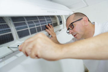 happy male technician repairing air conditioner with screwdriver