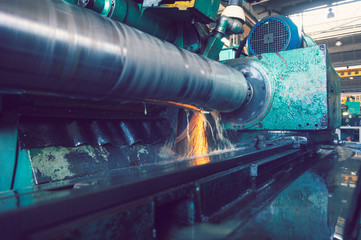 Grinding of the large shaft on the machine, finishing of the large round part, wide-angle toned photo.