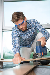 young man carpenter builder working with electric jigsaw and wood