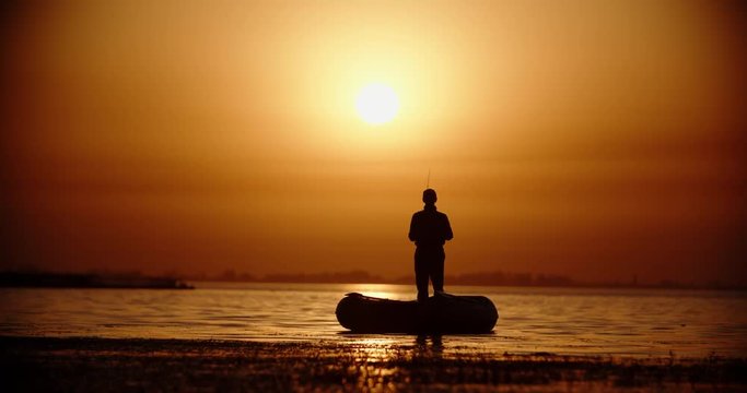 Professional fisherman trying to catch a fish with spinning rod in a rubber boat. lake in golden sunset 4k