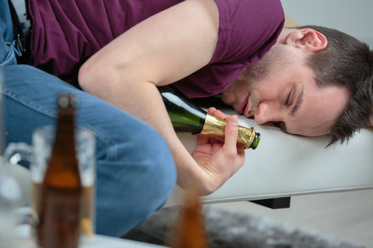 Inebriated man asleep holding empty wine bottle