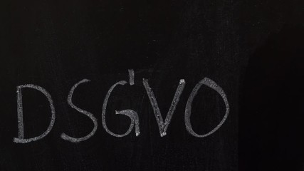 male hand writes a check mark behind the letters DSGVO on a black chalkboard